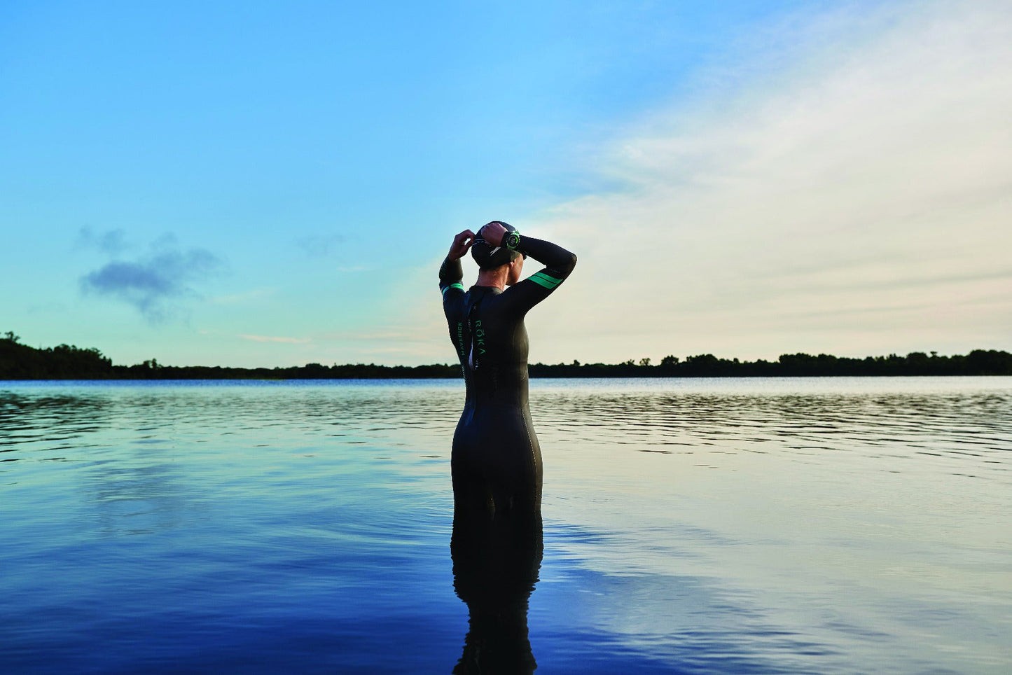 Garmin Forerunner 745 Neo Tropic smartwatch worn by a swimmer standing in a calm lake